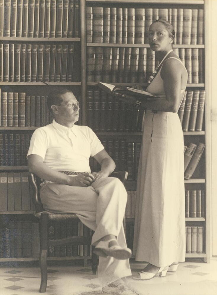  Feuchtwanger sitting in front of two bookshelves in his library in Sanary, with Marta standing next to him, 1933-1939. USC Digital Library. Lion Feuchtwanger Papers Collection.